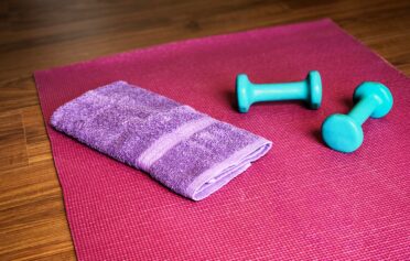 Purple towel and teal dumbbells on a red yoga mat.
