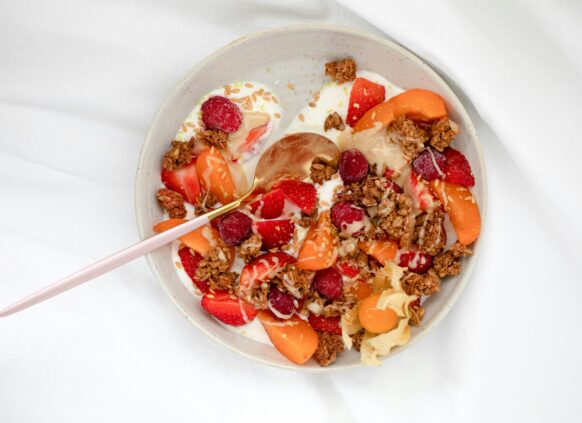 Bowl of yogurt topped with granola, strawberries, raspberries, melon, and flax seeds