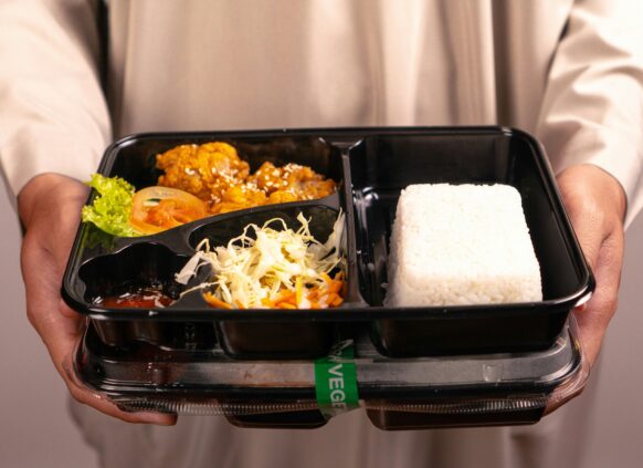 Person holding a bento-style meal box with rice, salad, and cooked vegetables
