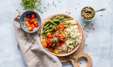 Healthy plate with salmon, green beans, cherry tomatoes, cauliflower rice, and pesto on a light blue background