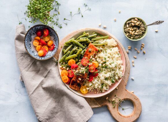 Healthy plate with salmon, green beans, cherry tomatoes, cauliflower rice, and pesto on a light blue background