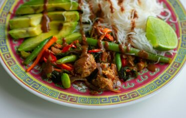 Colorful plate of Asian-inspired vegan stir-fry with green beans, noodles, avocado, and lime