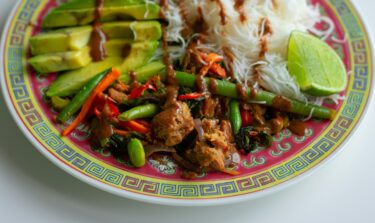 Colorful plate of Asian-inspired vegan stir-fry with green beans, noodles, avocado, and lime