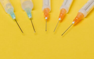 Multiple retatrutide syringes with orange and blue caps on a yellow background