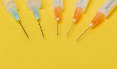 Multiple retatrutide syringes with orange and blue caps on a yellow background
