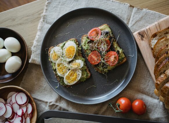 Healthy breakfast with avocado toast topped with eggs, tomatoes, and sprouts