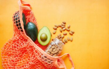 Avocados and almonds in a reusable net bag on an orange background.