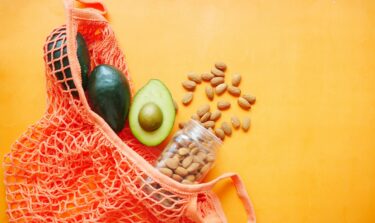 Avocados and almonds in a reusable net bag on an orange background.