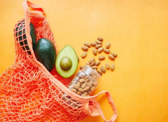 Avocados and almonds in a reusable net bag on an orange background.