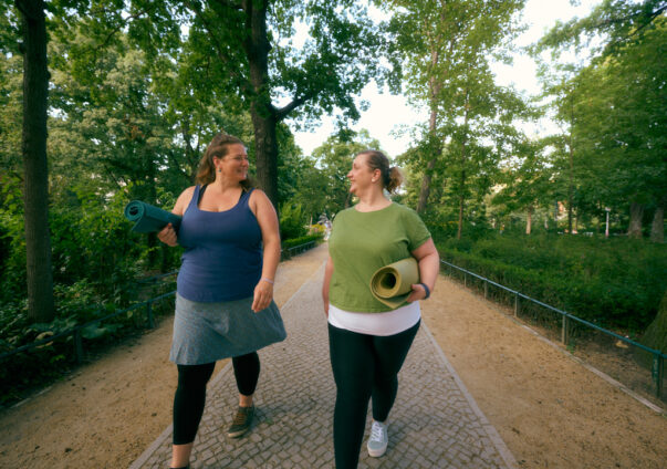 Two women walking in the park with yoga mats