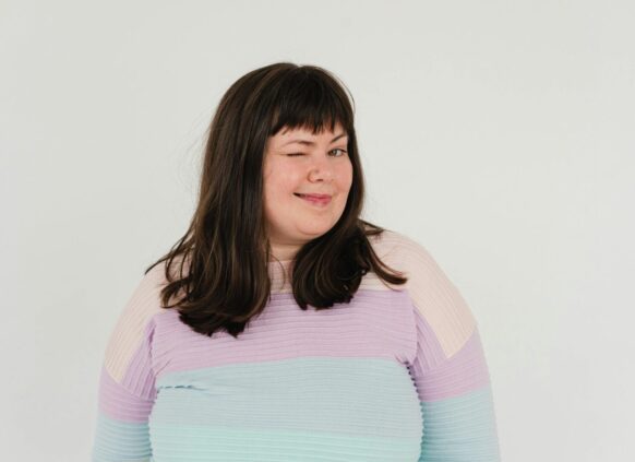 Plus size woman winking wearing pastel sweater on white background