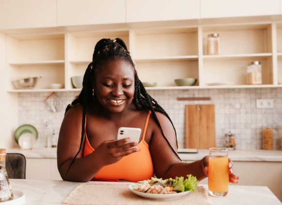 Woman sat with a meal and drink, smiling at her phone