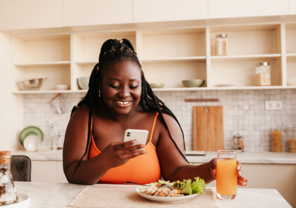 Woman sat with a meal and drink, smiling at her phone