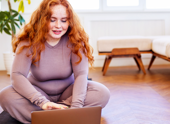 Overweight woman sitting on the floor, looking at her laptop