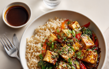 Bowl full of healthy tofu brown rice stir fry, with side of soy sauce