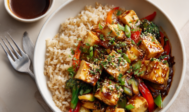 Bowl full of healthy tofu brown rice stir fry, with side of soy sauce