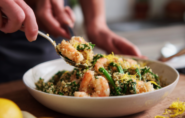 A hand spooning a prawn from a bowl of garlic prawn quinoa