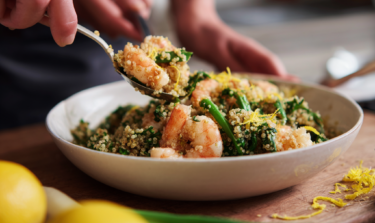 A hand spooning a prawn from a bowl of garlic prawn quinoa